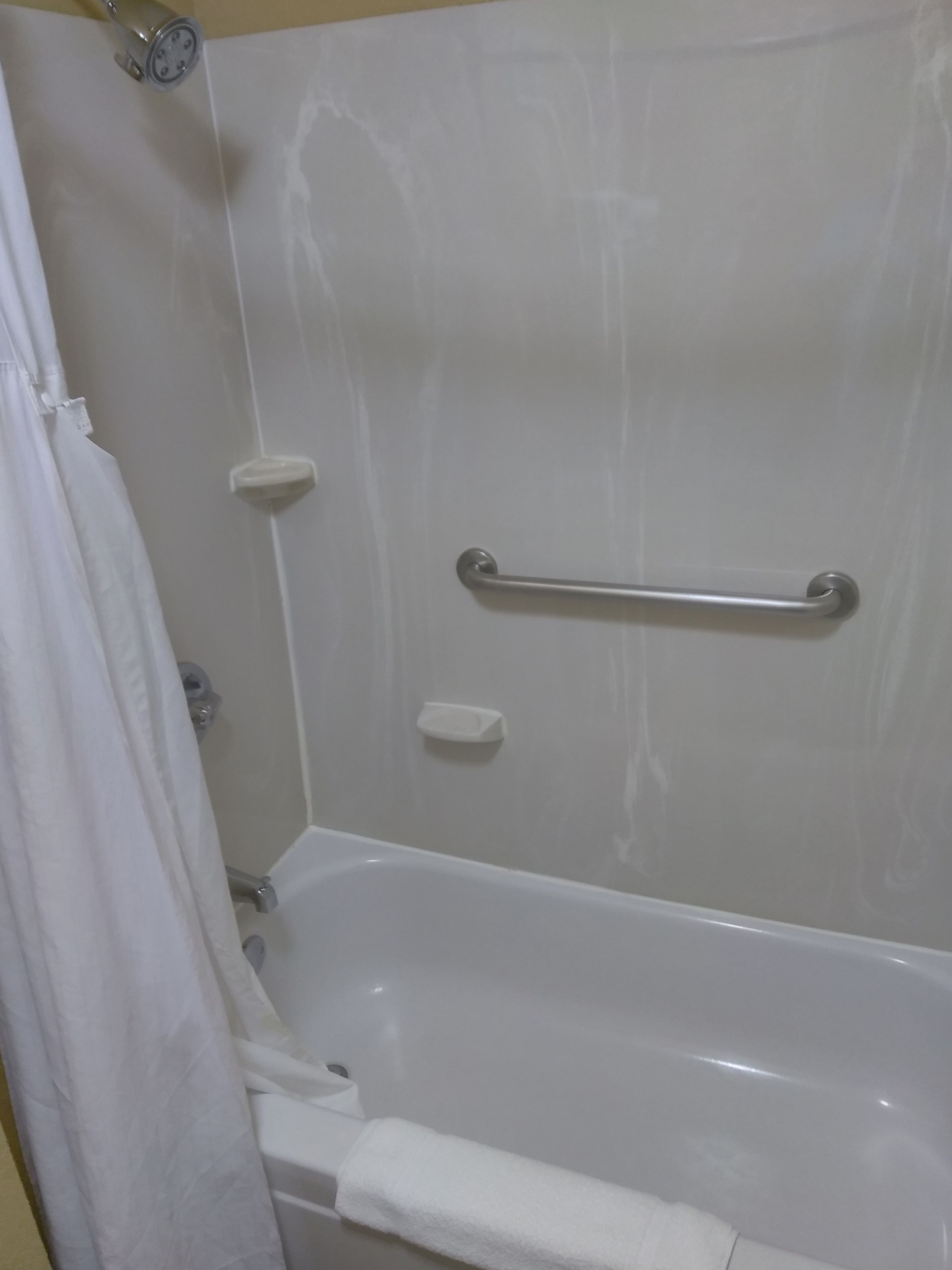 Eine weiße Badewanne mit einer Haltestange, einer Duschvorhang und einem Handtuchhalter.