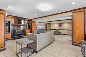 A hotel lobby with a fireplace, seating area, and a kitchenette.