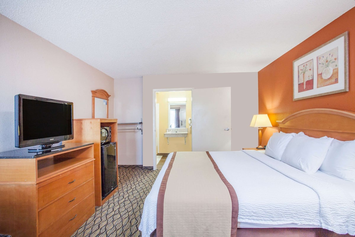 Ein Hotelzimmer mit Bett, Fernseher, Mikrowelle, Kommode und einem durchgegangenen Tür sichtbaren Badezimmer.