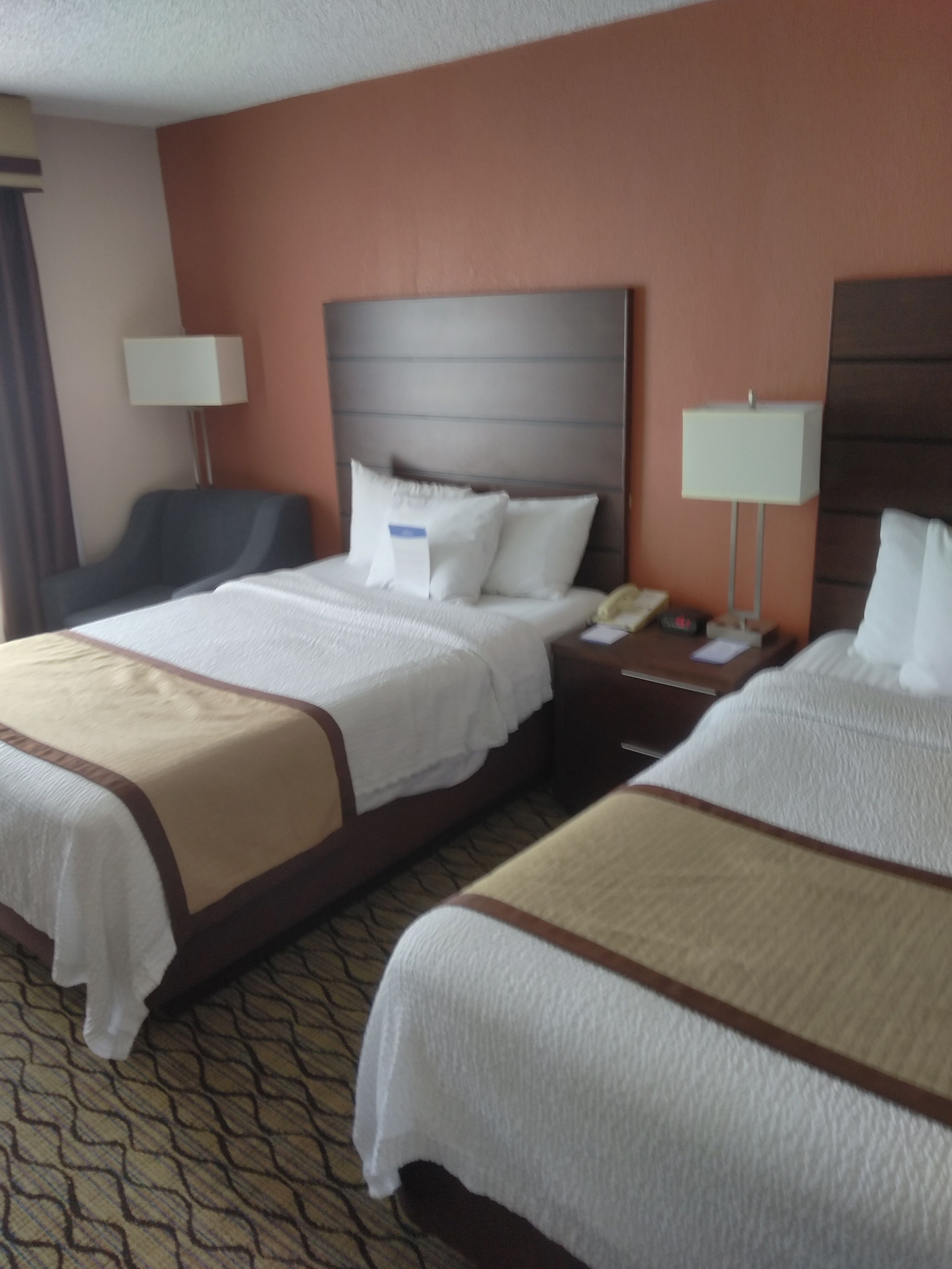 A hotel room with two beds, a desk, a chair, and a lamp.