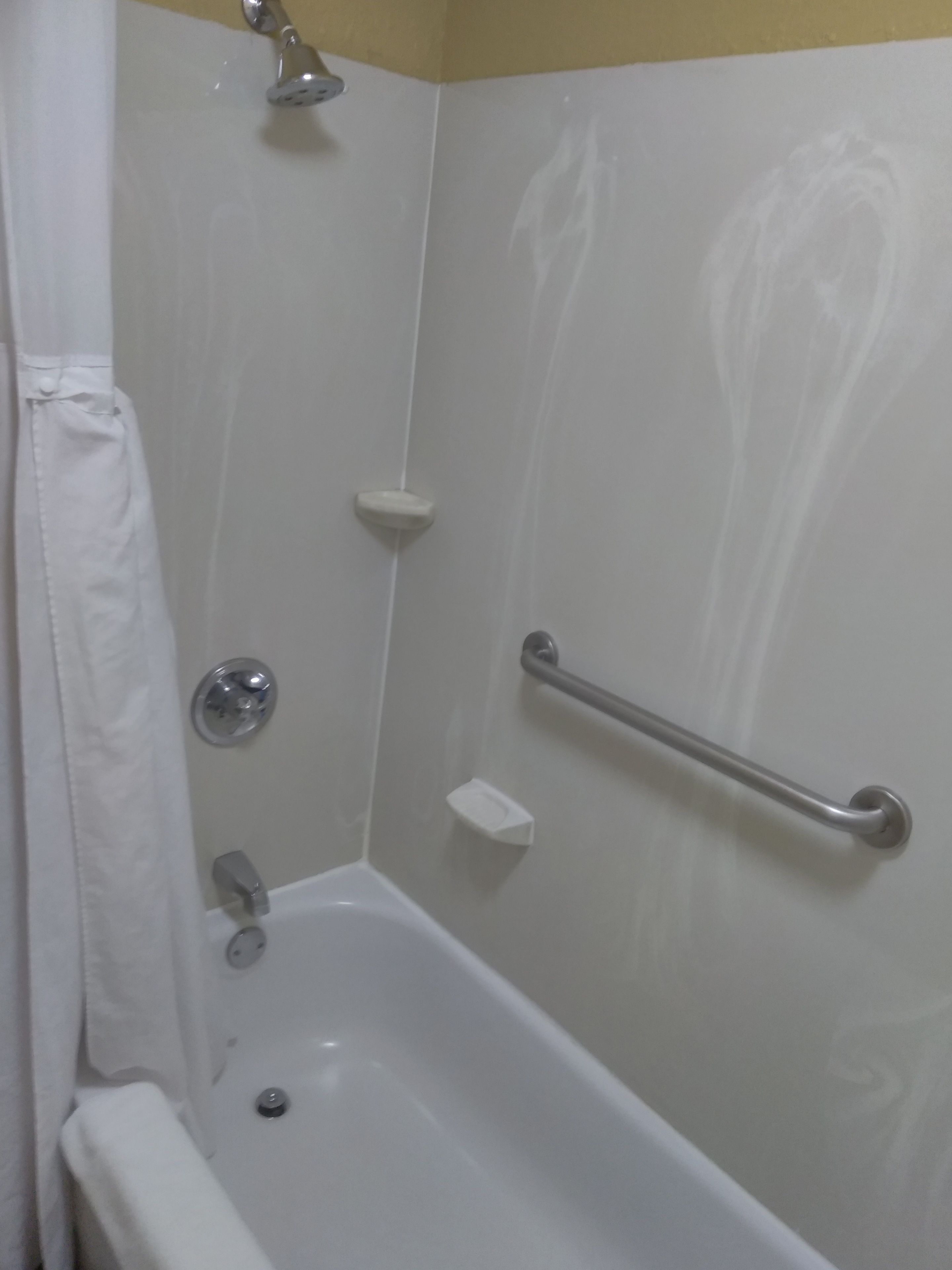 A white bathtub with a showerhead, a grab bar, and a small shelf.