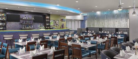 A restaurant with multiple tables, chairs, a bar area, and a decorative wall.