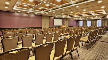 Un salón de conferencias con filas de sillas, una pantalla de proyector y un atril.