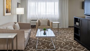 A hotel room with a sofa, armchair, small table, TV, and a patterned carpet. - Crowne Plaza Kitchener-Waterloo by IHG (Kitchener)
