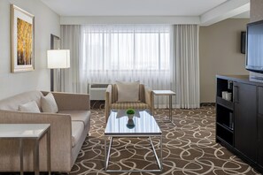 Une chambre d’hôtel équipée d’un canapé, d’un fauteuil, d’une petite table, d’une télévision et d’un tapis à motifs.