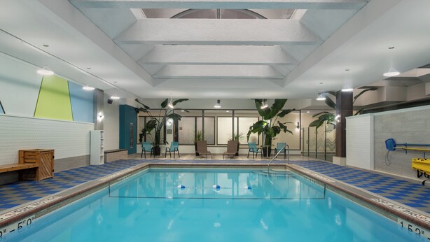 An indoor swimming pool with a checkered floor, ceiling lights, and potted plants. - Crowne Plaza Kitchener-Waterloo by IHG (Kitchener)