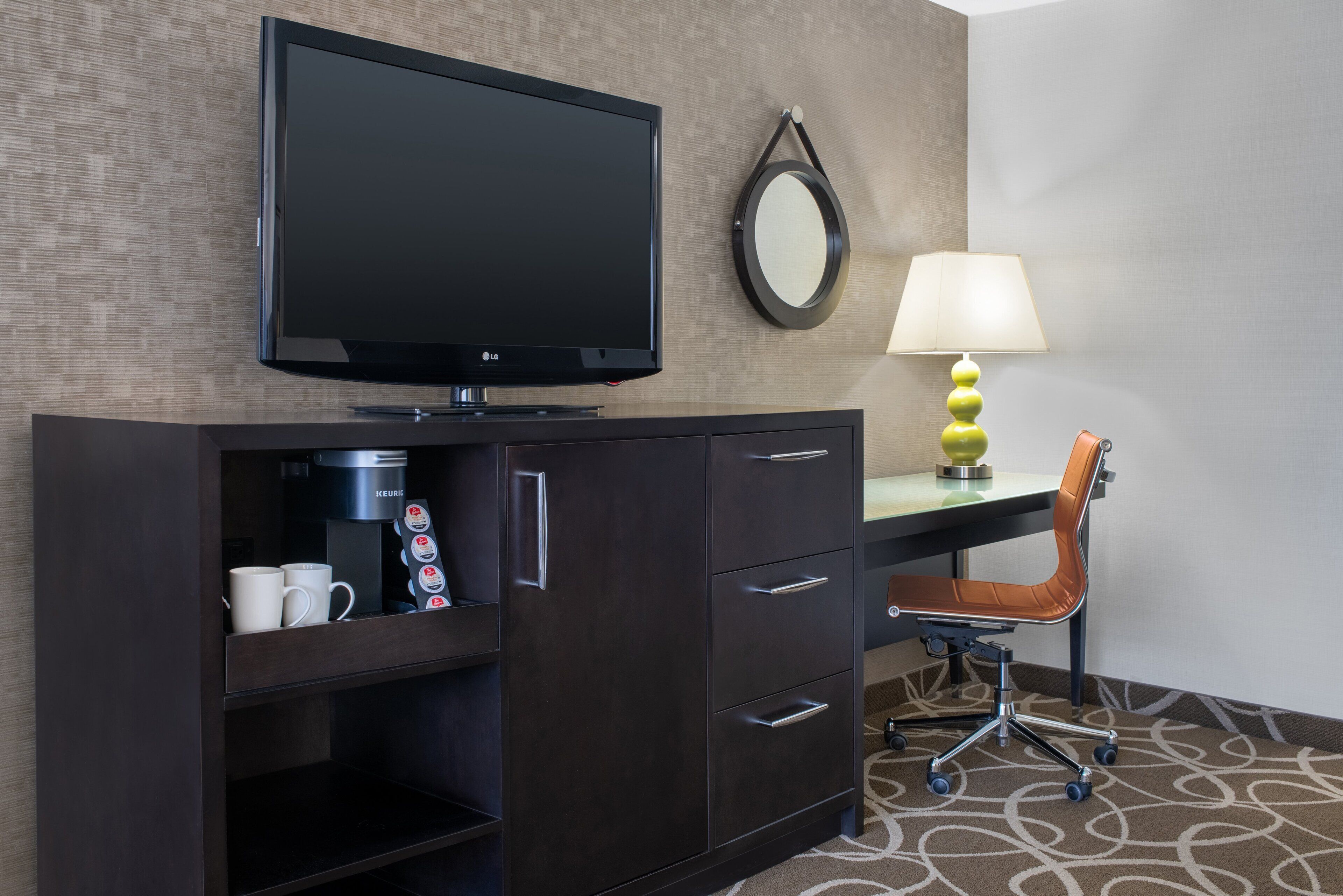 Une chambre d’hôtel équipée d’une télévision, d’une machine à café, d’un bureau avec une chaise et d’une lampe.