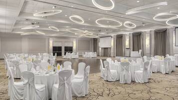 Un salón de banquetes con mesas redondas, sillas blancas y una pantalla grande.