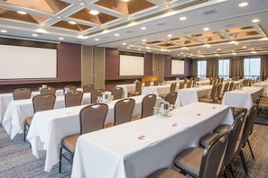 A conference room with multiple tables, chairs, and a presentation screen.