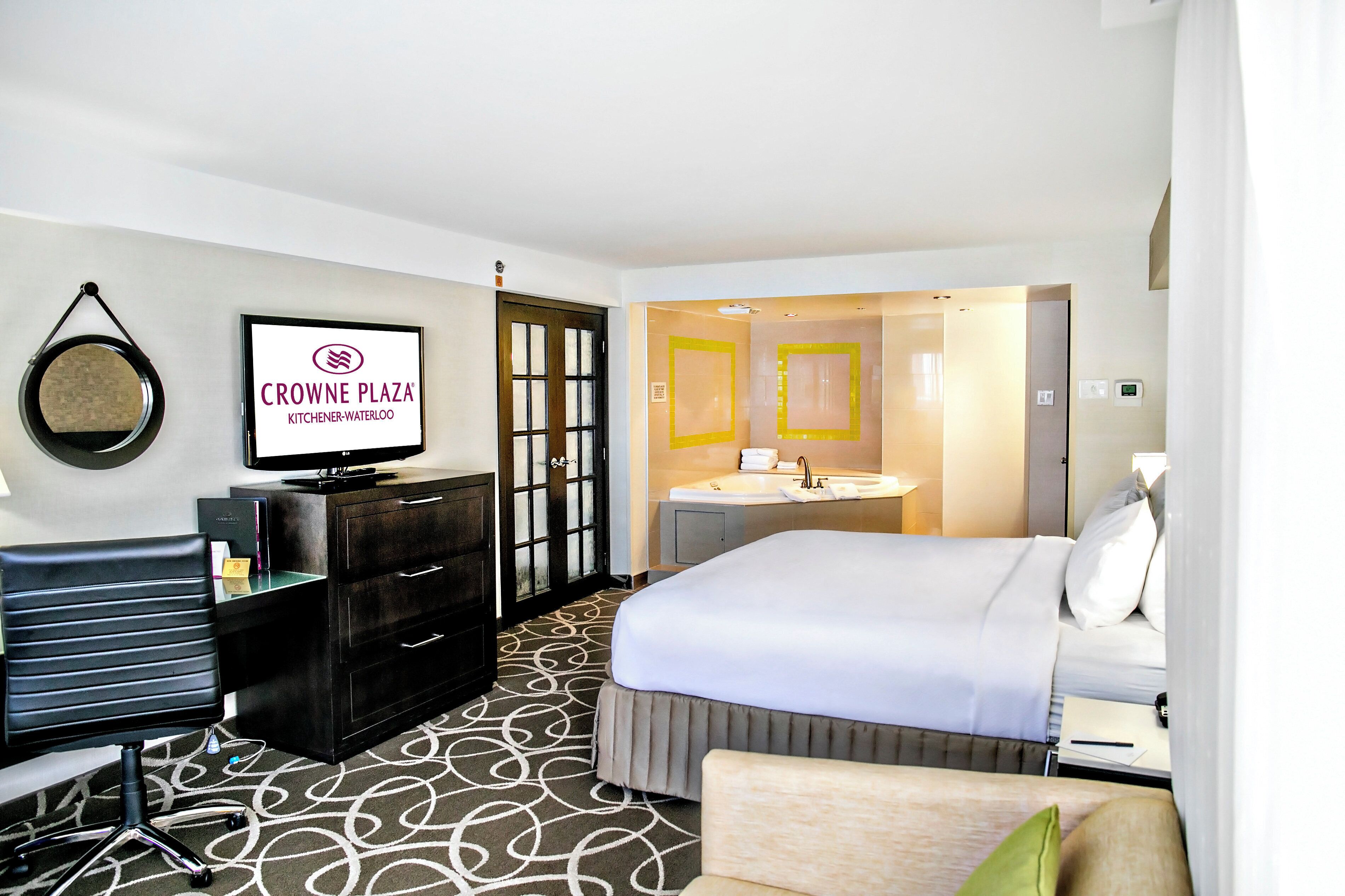 Una habitación de hotel con una cama, un escritorio, un aparador, un espejo y un cartel que dice 'Crowne Plaza Kitchener-Waterloo'.
