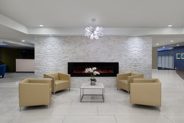 A modern lobby with a stone wall, a fireplace, and two beige sofas around a glass coffee table. - Crowne Plaza Kitchener-Waterloo by IHG (Kitchener)