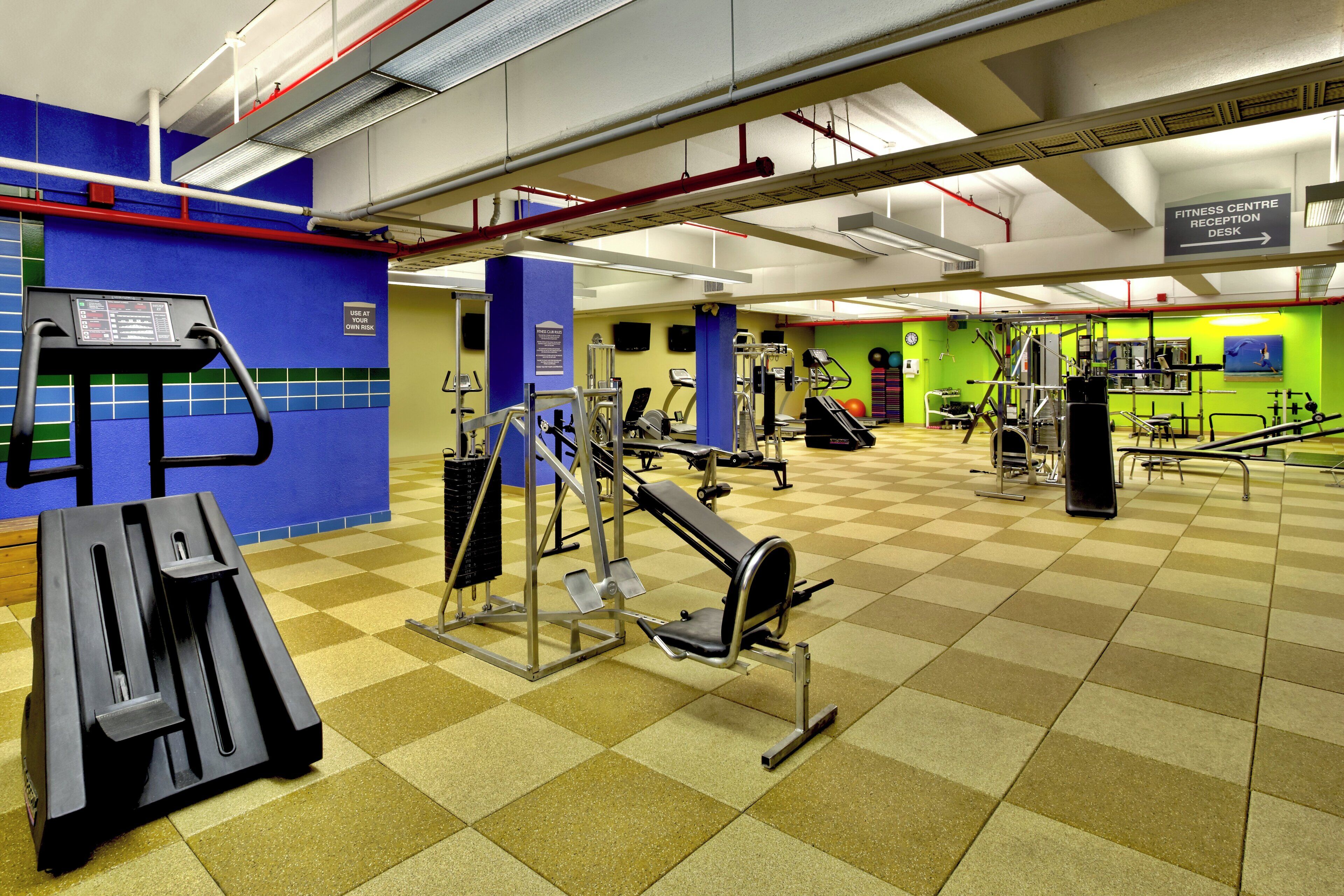 Uma academia com diversos equipamentos de exercícios, um balcão de recepção e um relógio na parede.