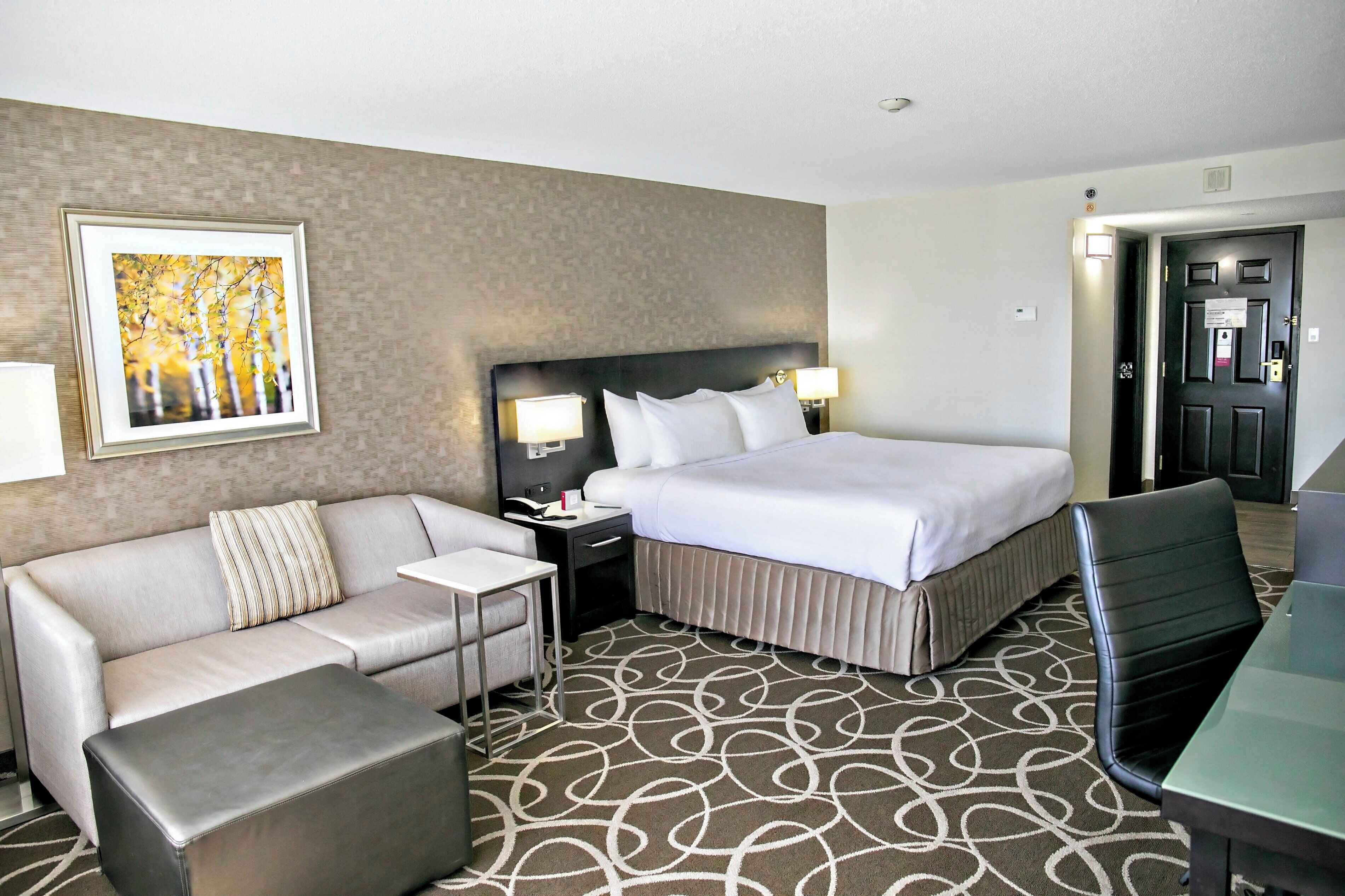 Een hotelkamer met een bed, een bank, een kleine tafel, een stoel en een vloerkleed met een geometrisch patroon.