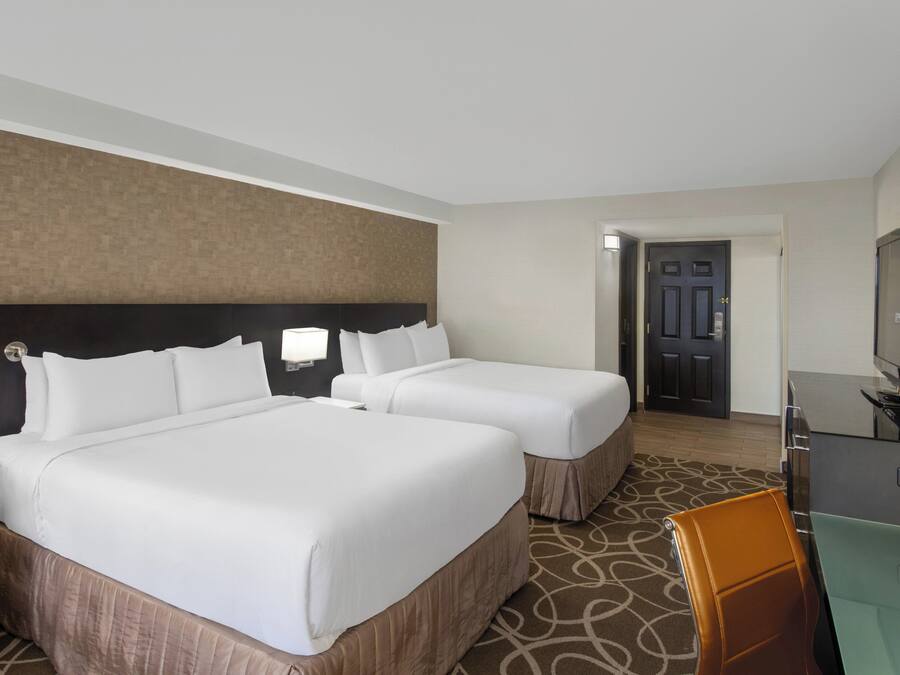 A hotel room with two beds, a desk with a television, and a door leading to another room.