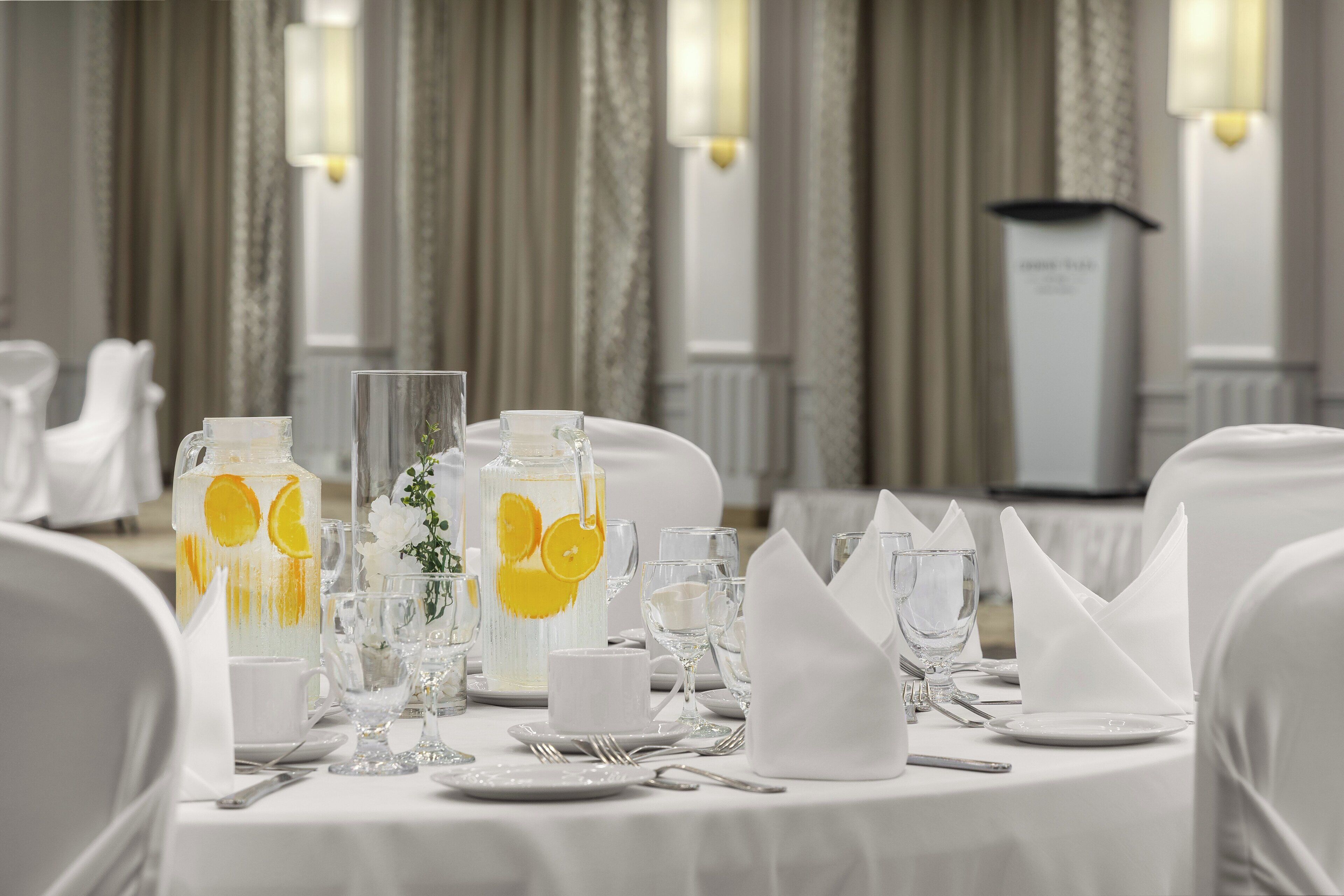 A table set for a formal event with clear glassware, a pitcher with citrus slices, and a microphone stand in the background.