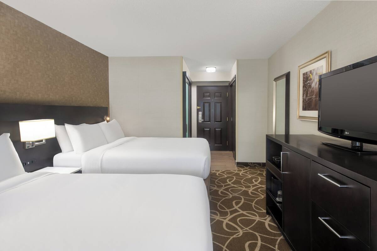 A hotel room with two beds, a TV, a desk, and a door leading to a hallway.