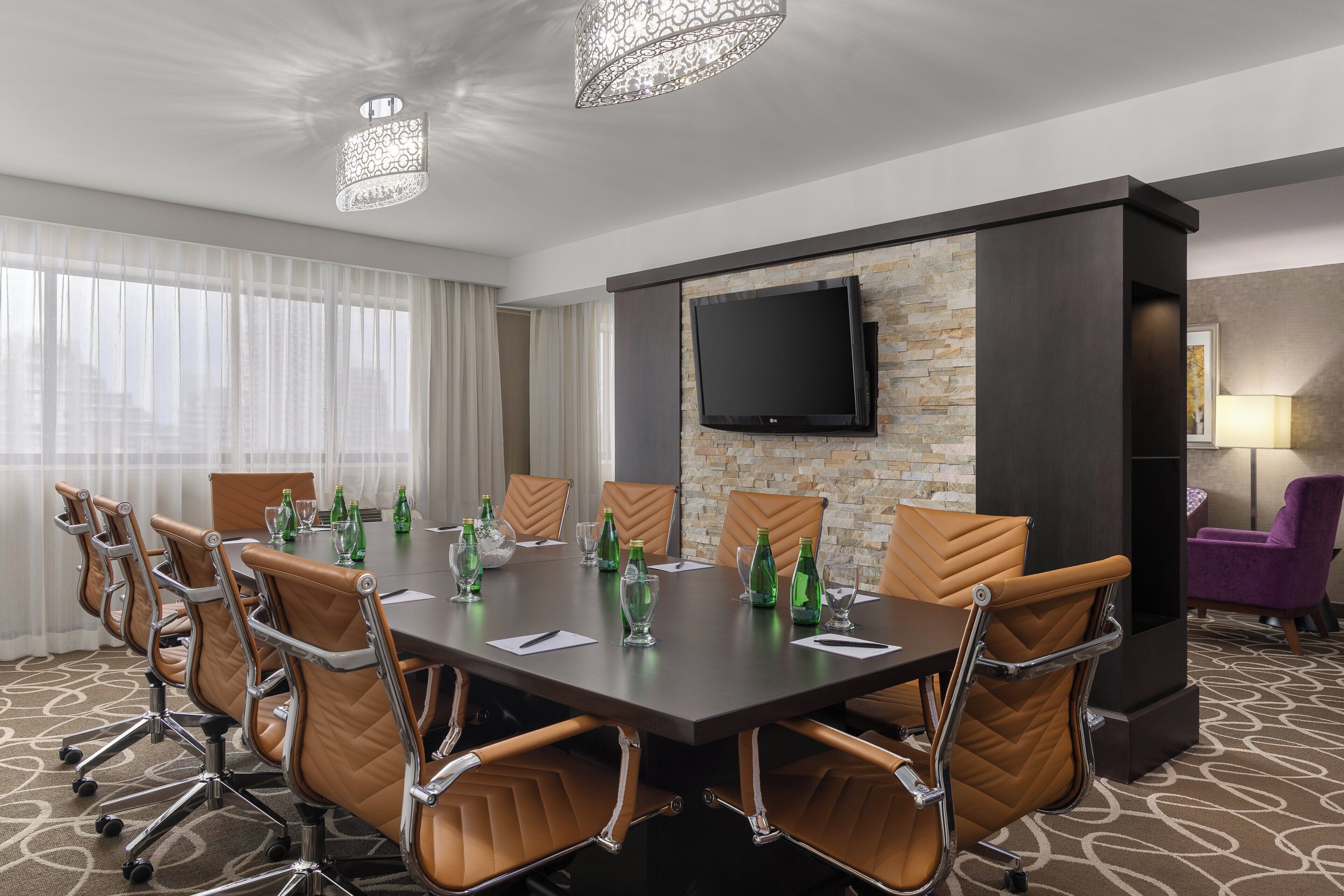 A conference room with a large table, chairs, a flat-screen TV, and a stone wall.