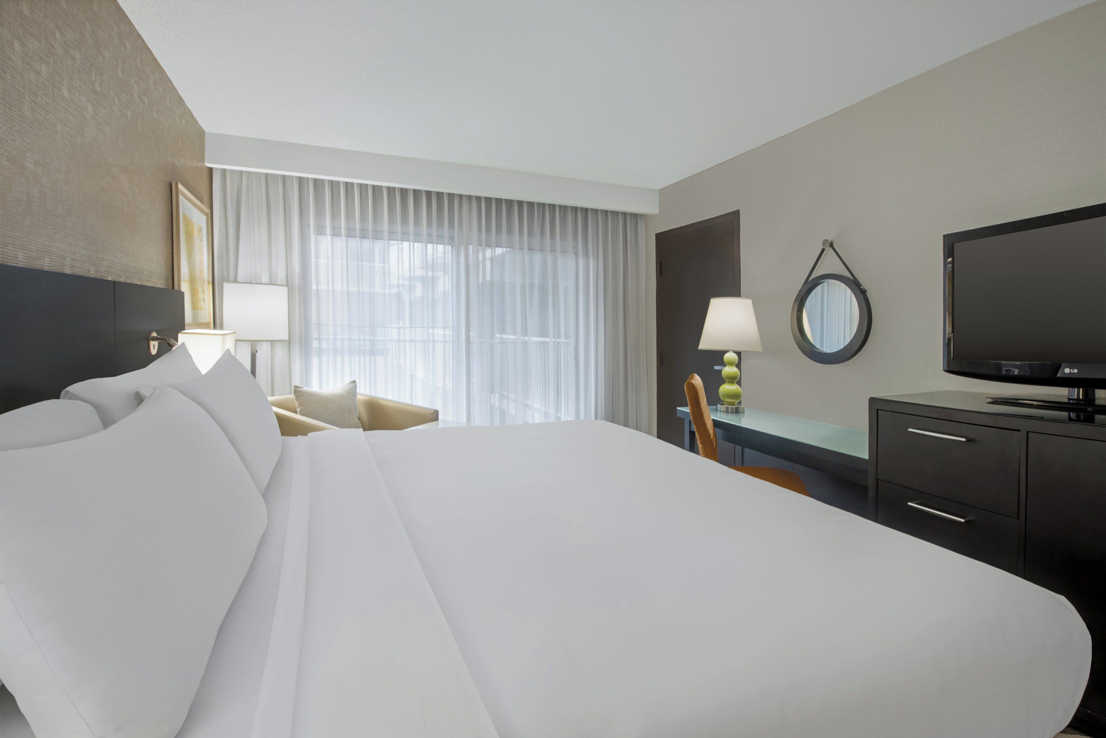 Habitación de hotel con una cama grande, un escritorio, una silla, un televisor y una ventana con cortinas.