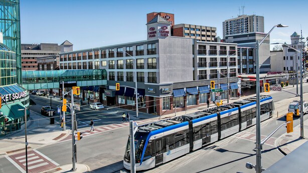 A modern building with a prominent clock tower, a tram line, and a pedestrian crossing.