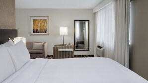 A hotel room with a large bed, a sofa, a small table, a lamp, a painting, a mirror, and a window with curtains. - Crowne Plaza Kitchener-Waterloo by IHG (Kitchener)
