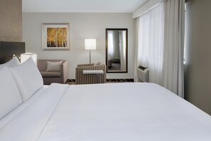 Une chambre d’hôtel avec un grand lit, un canapé, une petite table, une lampe, un tableau, un miroir et une fenêtre avec des rideaux.