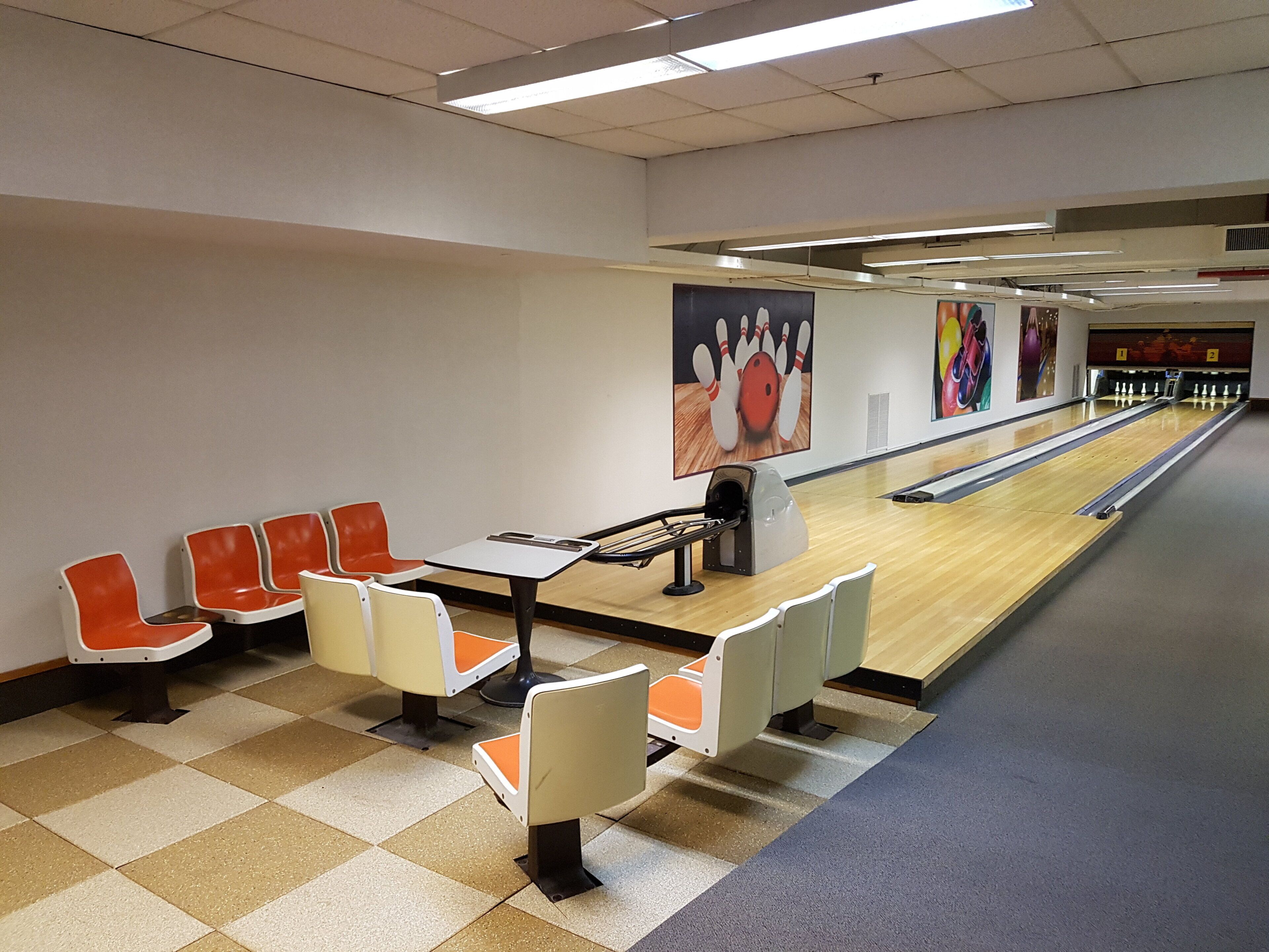 Een bowlingbaan met oranje en witte zitplaatsen, een bowlingbaan en een neerzetapparaat voor de bowlingpinnen.