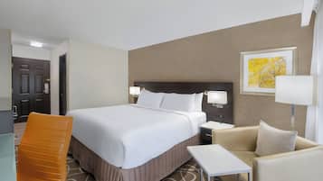 A hotel room with a bed, a chair, a small table, and a nightstand with a lamp.