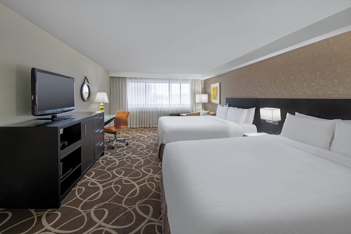 A hotel room with two beds, a TV, a desk, and a chair.