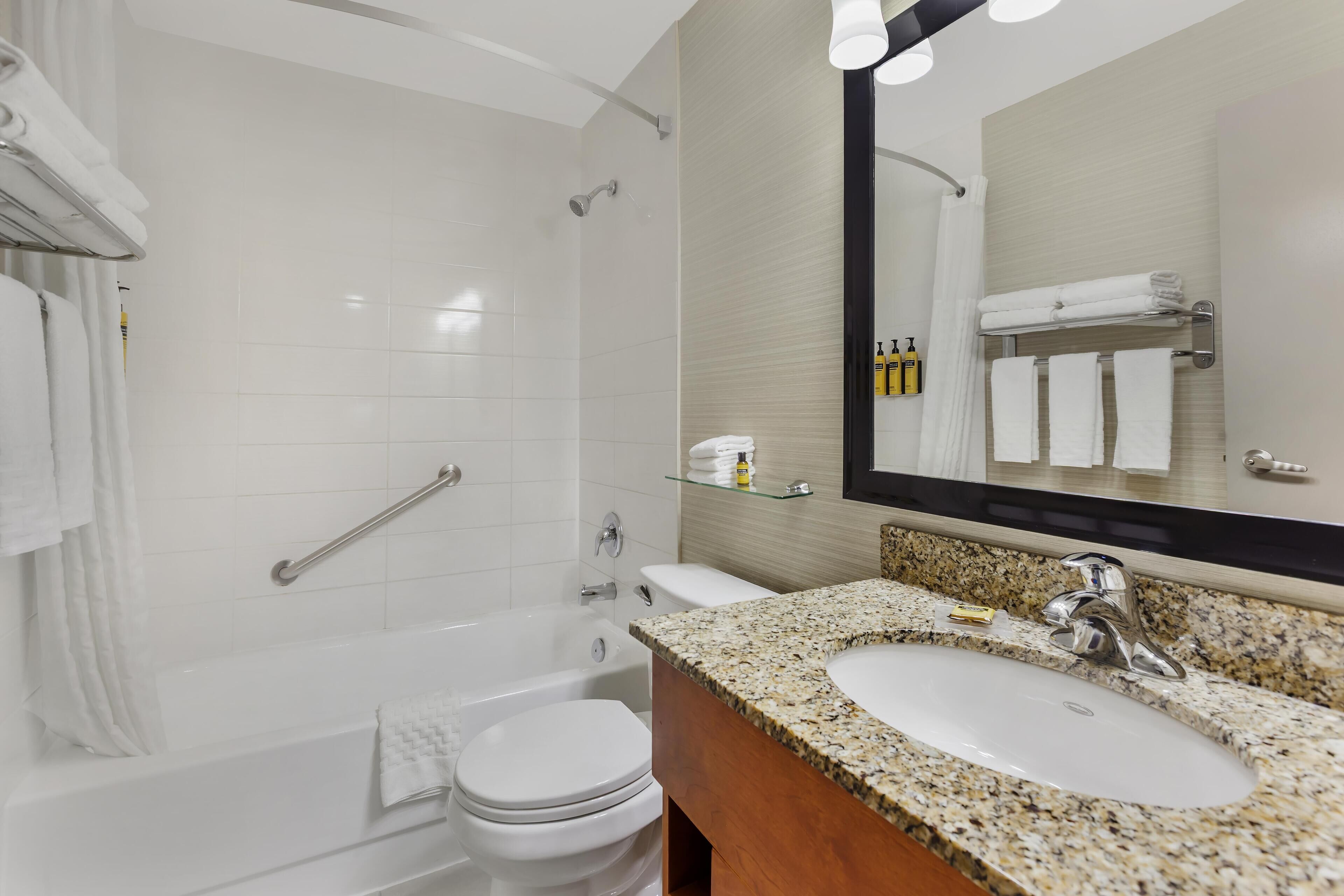 A modern bathroom with a white bathtub, a white toilet, a granite sink, and a large mirror.