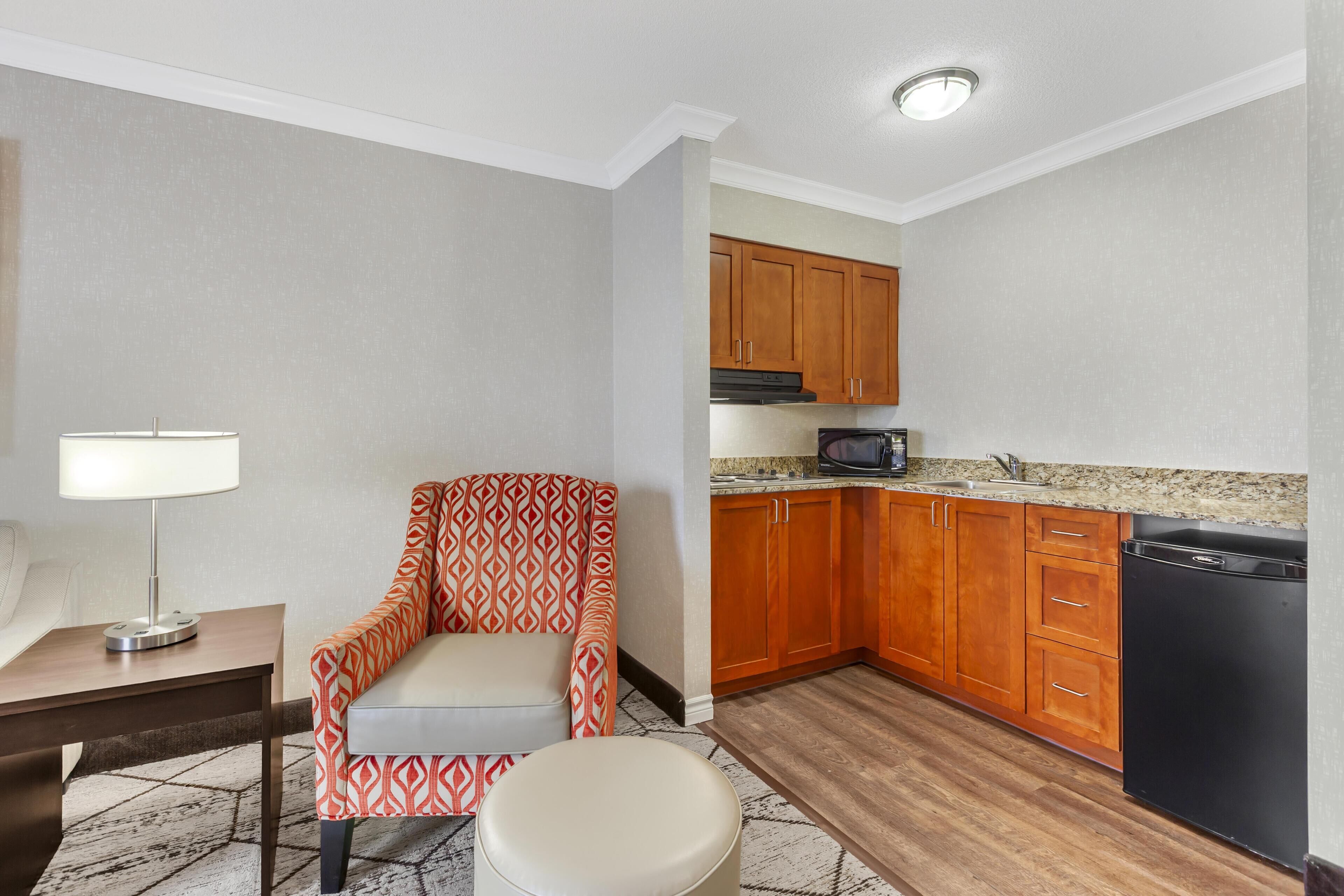 A compact living space with a kitchenette, a sofa, a small table, and a lamp.