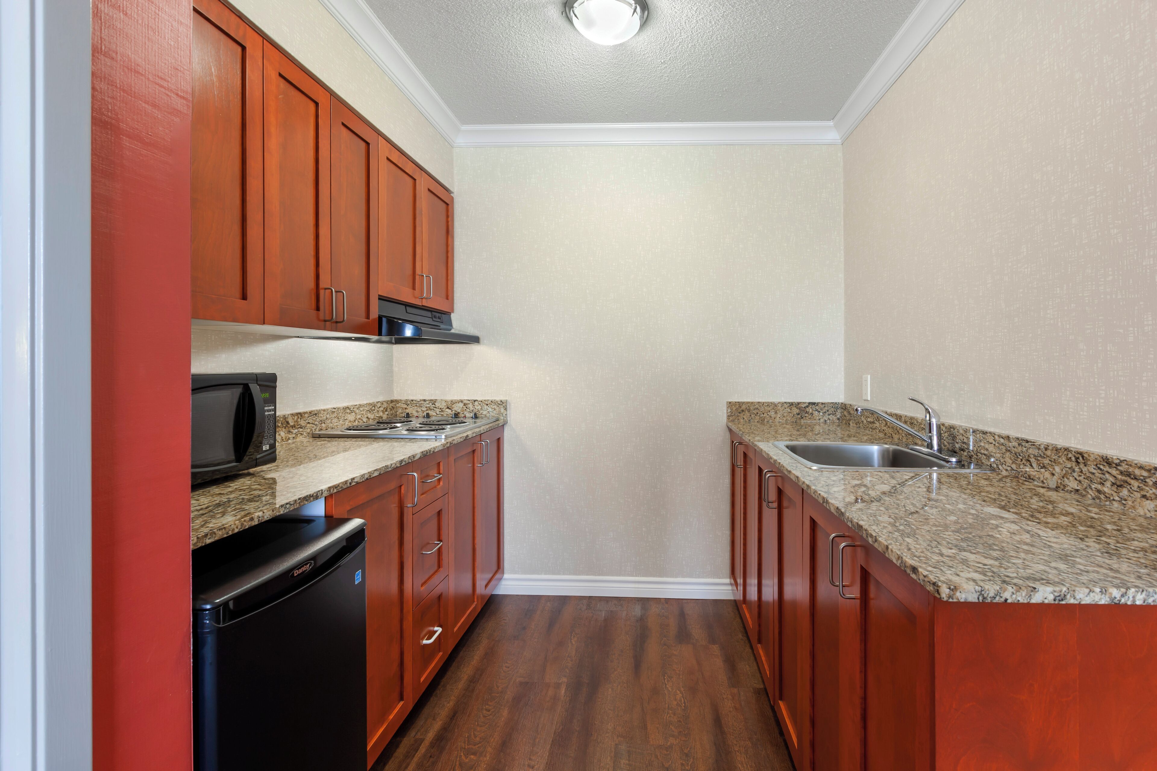 A compact kitchen with wooden cabinets, a granite countertop, a built-in microwave, and a dishwasher.