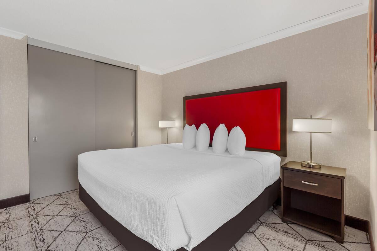 A hotel room with a large bed, a red headboard, two bedside tables with lamps, and a patterned floor.