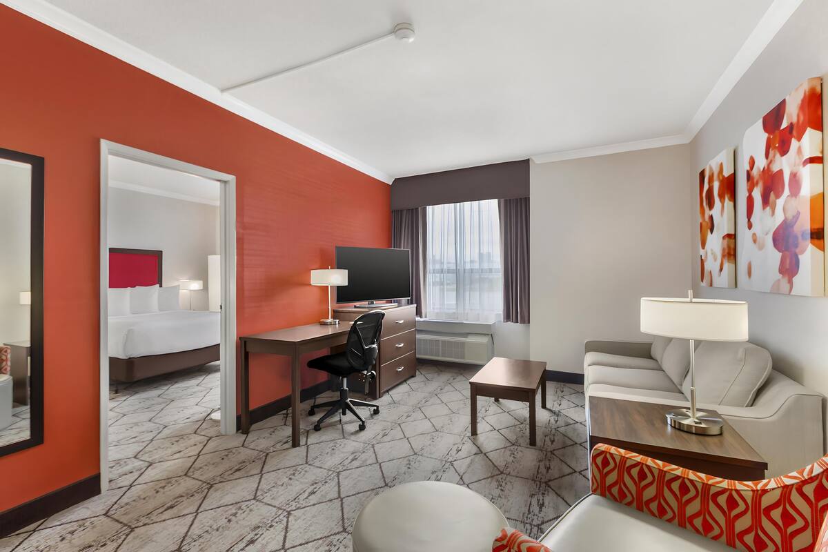 A hotel room with a bed, desk, chair, sofa, and a TV.