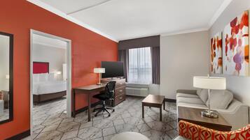 A hotel room with a bed, desk, chair, sofa, and a TV.