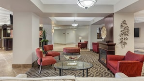 A spacious lobby with a modern design, featuring a glass coffee table, red upholstered chairs, and a fireplace. - Best Western Plus Rose City Suites (Welland)