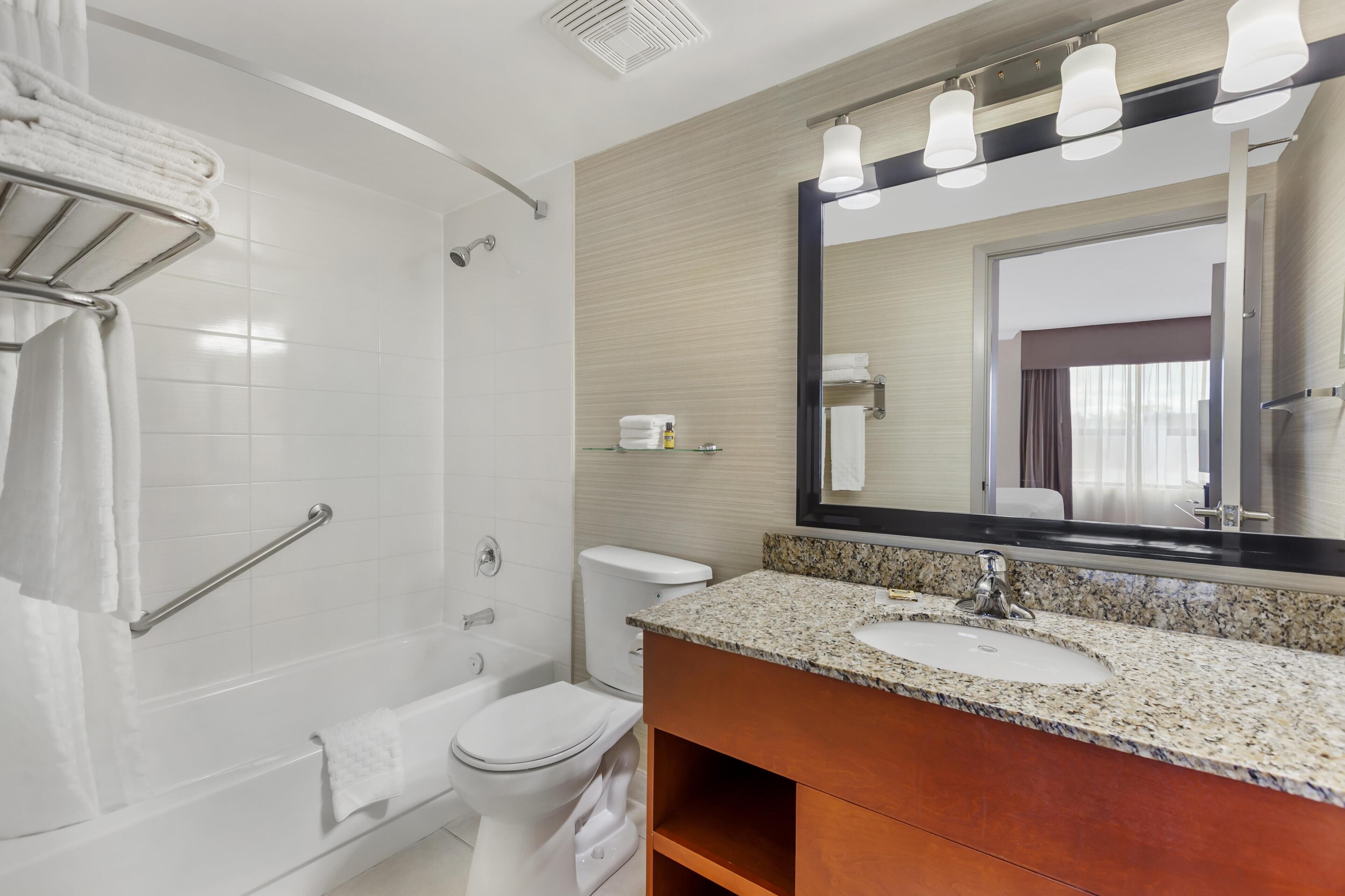 Une salle de bain moderne avec des toilettes blanches, une douche, un meuble-lavabo avec un plan de travail en granit et un grand miroir.