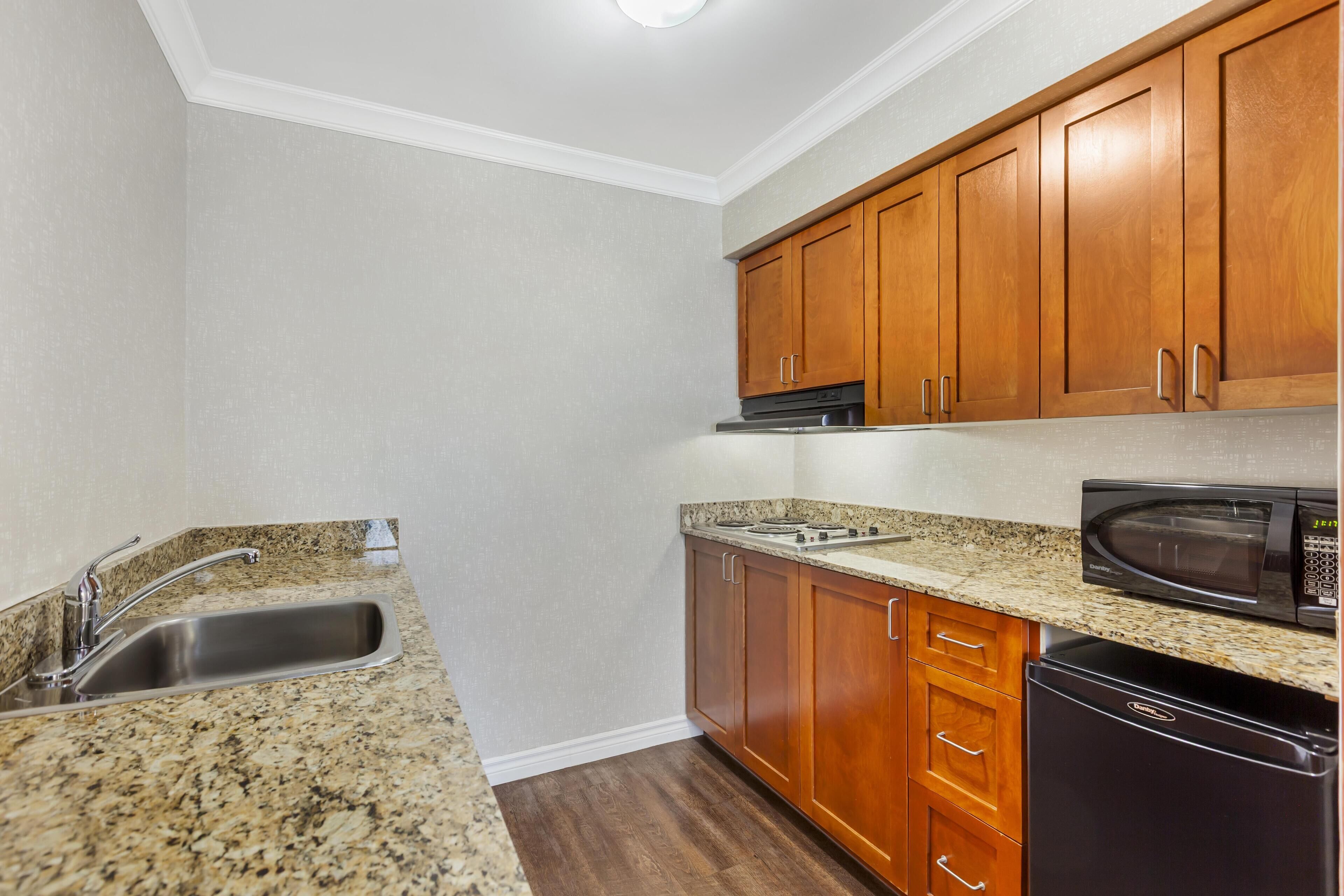 A kitchen with granite countertops, wooden cabinets, a stainless steel sink, a microwave, and a dishwasher.