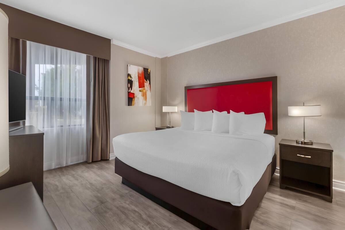 A modern hotel room with a large bed, a TV, a desk, and a window with curtains.