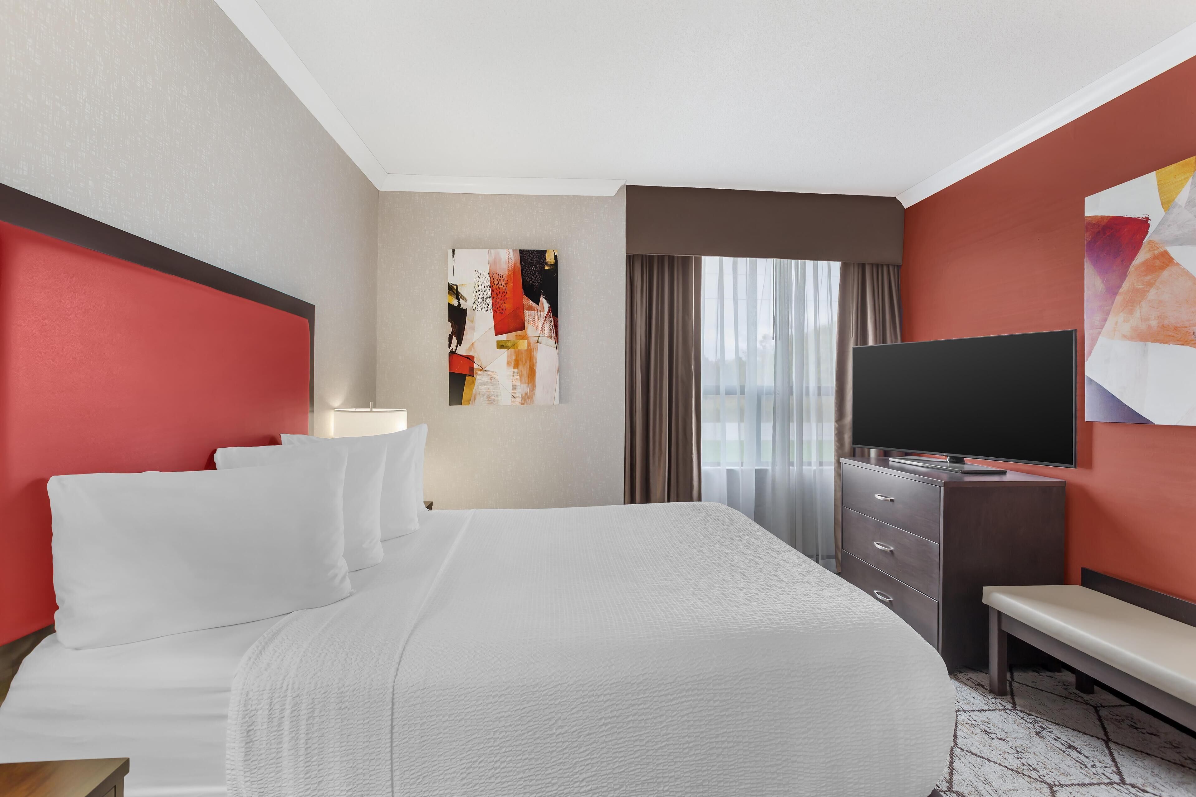 Een hotelkamer met een groot bed, een televisie, een bureau en een bankje.