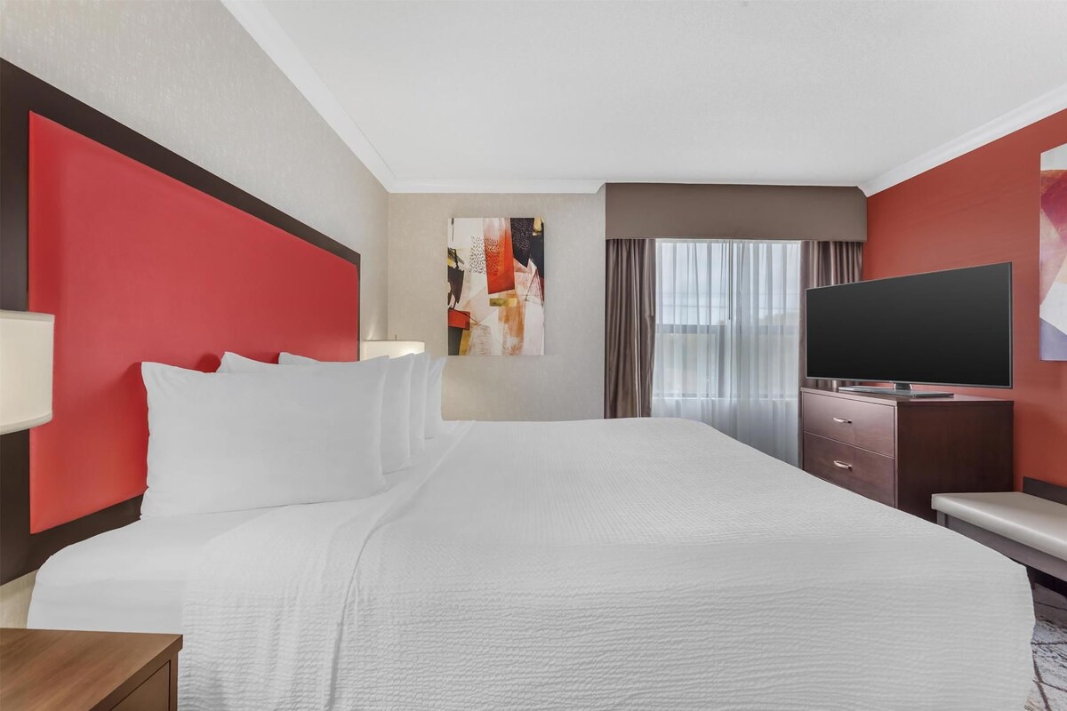 Una habitación de hotel con una cama grande, televisión de pantalla plana, escritorio y ventana con cortinas.