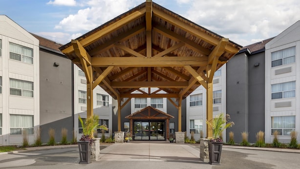 A hotel entrance with a wooden pavilion, large windows, and potted plants. - Best Western Plus Rose City Suites (Welland)
