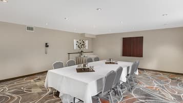 Uma sala de conferências com uma mesa comprida, cadeiras, toalha de mesa branca, cantinho de café e carpete estampado.