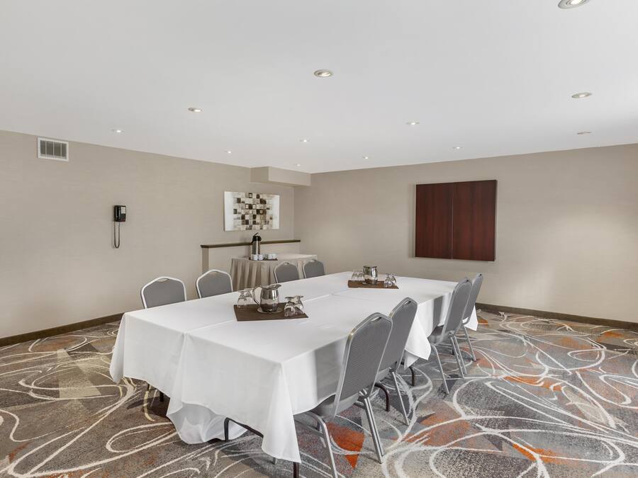 Uma sala de conferências com uma mesa comprida, cadeiras, toalha de mesa branca, cantinho de café e carpete estampado.