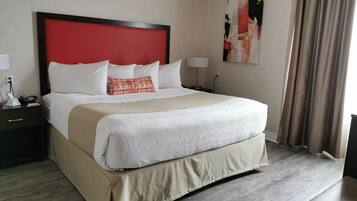 Hotelkamer met een groot bed, een rood hoofdbord, witte beddengoed, een beige accentkleur, een nachtkastje met een lamp en een schilderij aan de muur.