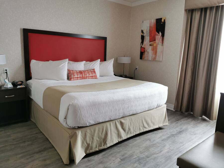 Hotelkamer met een groot bed, een rood hoofdbord, witte beddengoed, een beige accentkleur, een nachtkastje met een lamp en een schilderij aan de muur.