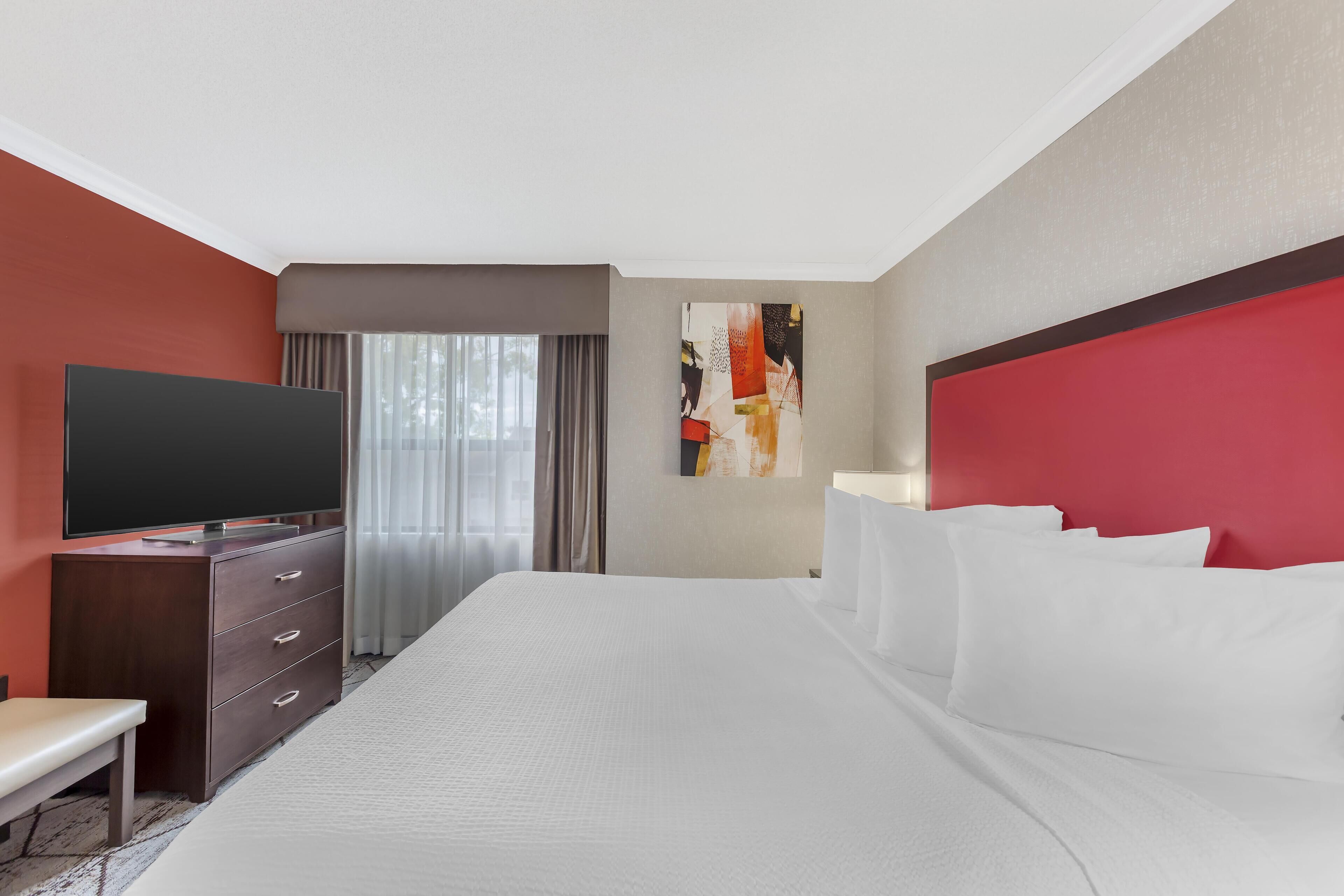 A hotel room with a large bed, a flat-screen TV, a desk, and a window with curtains.