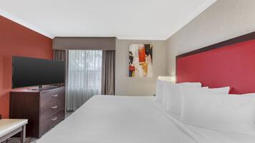 A hotel room with a large bed, a flat-screen TV, a desk, and a window with curtains.