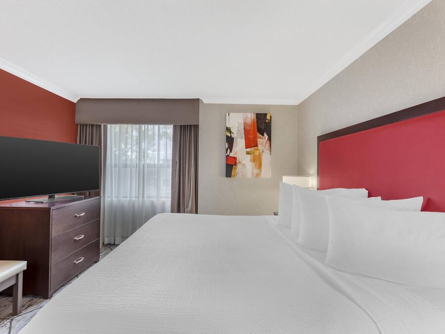 A hotel room with a large bed, a flat-screen TV, a desk, and a window with curtains.