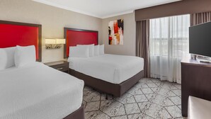 A hotel room with two beds, a TV, a desk, and a large window with curtains. - Best Western Plus Rose City Suites (Welland)