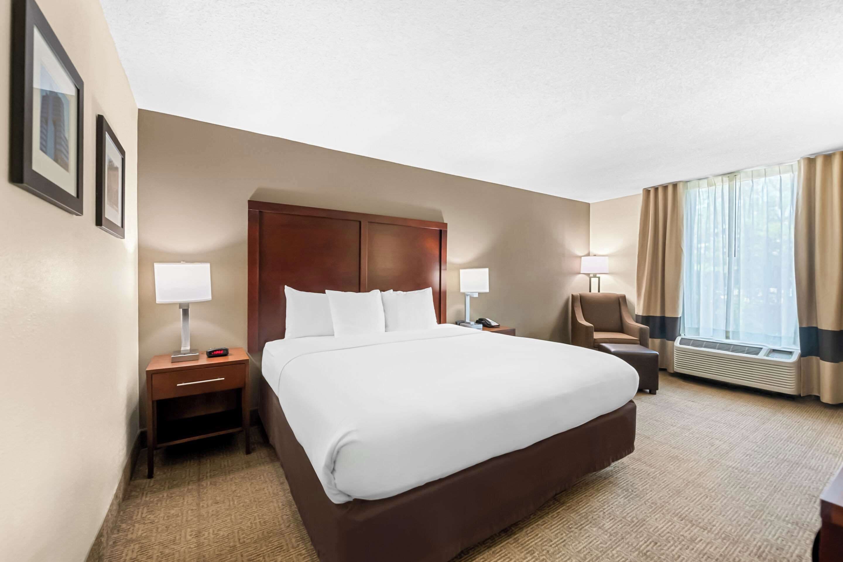 A hotel room with a large bed, two bedside tables with lamps, a chair, a desk, and a window with curtains.